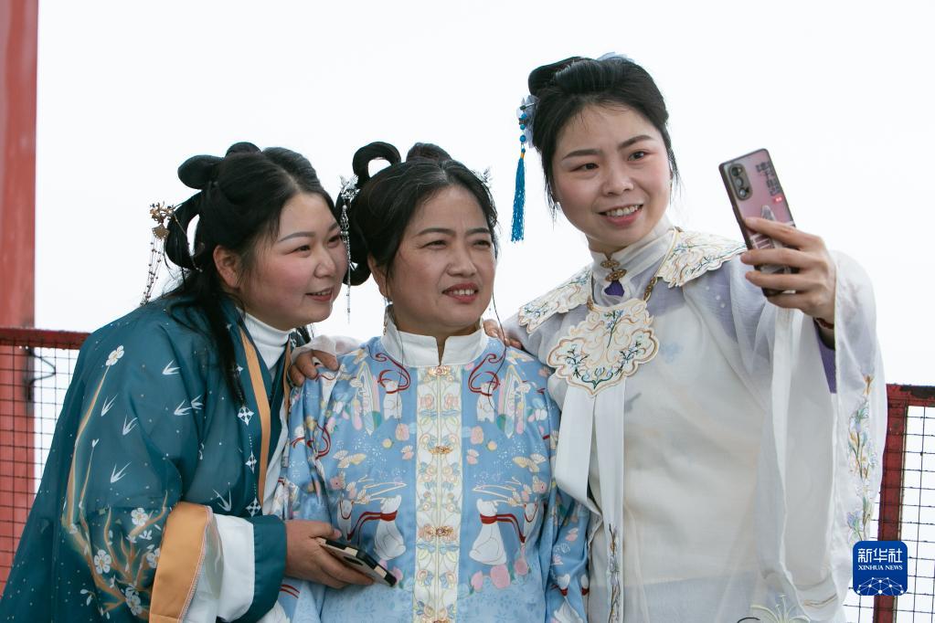 Tre operaie vestite con abiti tradizionali si scattano un selfie sul tetto della torre principale del progetto Chongqing Luhai International Centre. (7 marzo 2023 – Xinhua/Chu Jiayin)