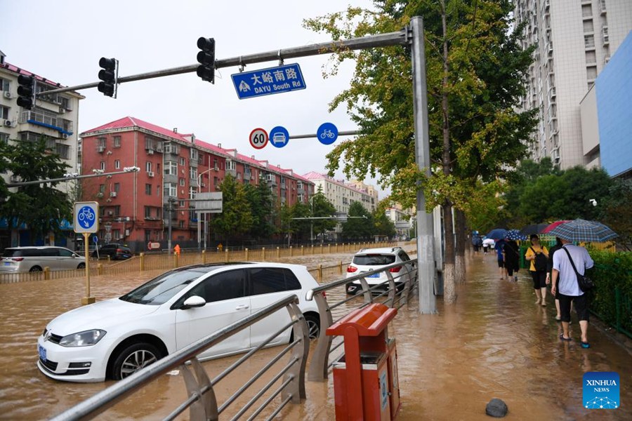 Passanti davanti alle auto sommerse dall'acqua nel distretto di Mentougou a Beijing. (31 luglio 2023 - Foto/Xinhua)