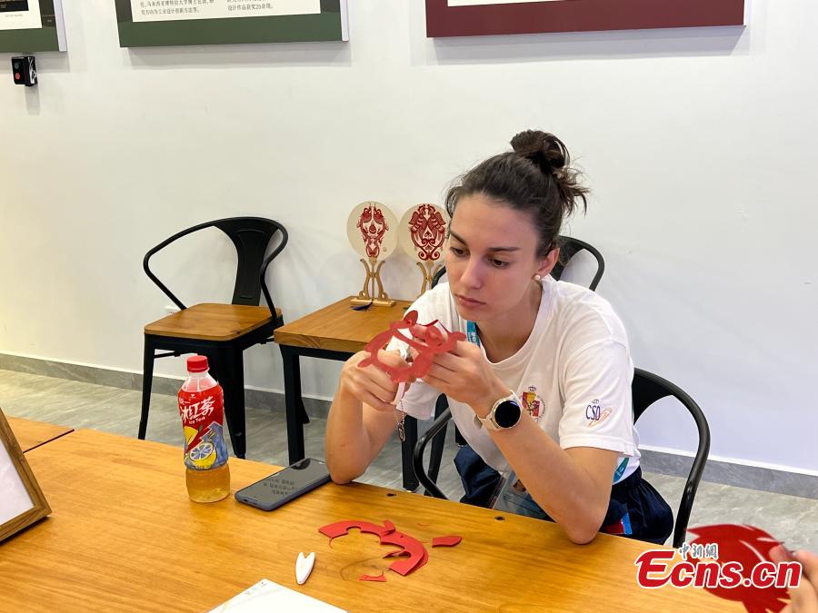 Un'atleta straniera impara l'arte cinese del ritaglio della carta al villaggio degli atleti delle Universiadi di Chengdu, nella provincia del Sichuan, nel sud-ovest della Cina. (2 agosto 2023 - China News Service/Cheng Jiaxin)